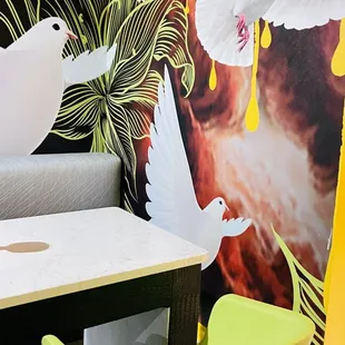 a table with two chairs and a wall with a mural of white doves