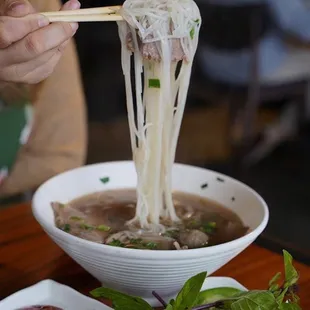 a person holding chopsticks above a bowl of soup