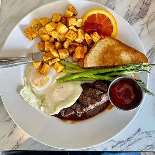 Steak and eggs with asparagus and home fries.