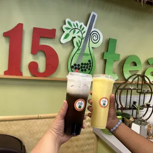 two people holding drinks in front of a sign