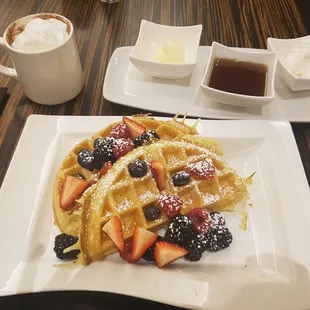 a plate of waffles with berries and powdered sugar