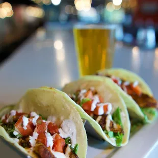 two tacos on a white plate with a glass of beer