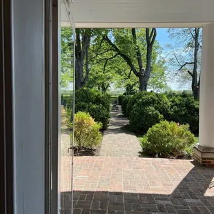 A view from inside the house looking outside. There is seating on either side of the house on the patio, as well as in the green area.