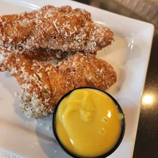 a plate of fried chicken strips with a side of mustard