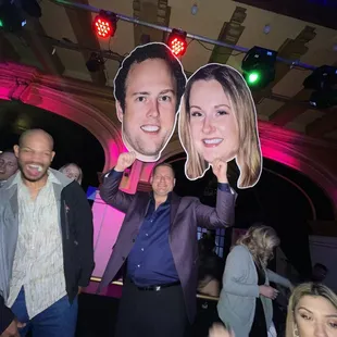 a man and a woman holding a cut out of a man&apos;s face