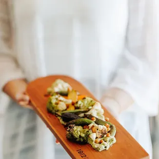 a woman holding a wooden platter with food on it