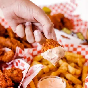 a person dipping a piece of chicken nuggies into a basket of fries