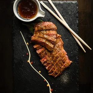 a piece of meat on a slate board with chopsticks and sauce