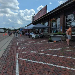 a brick paved street with people sitting at tables and umbrellas