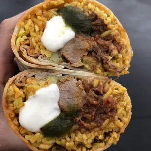 ows a hand holding a burrito with meat and rice