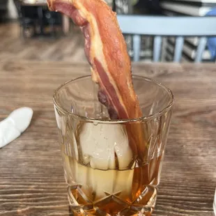 a glass of whiskey with a bacon stick sticking out of it