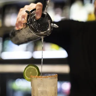 a bartender pouring a margarita into a glass