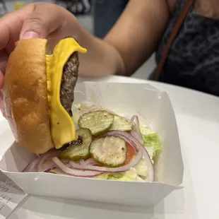 a hand holding a hamburger with cheese and pickles