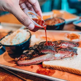 a hand drizzling barbecue sauce over a plate of meat