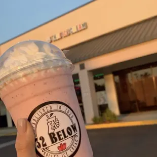 a hand holding a pink drink with whipped cream on top