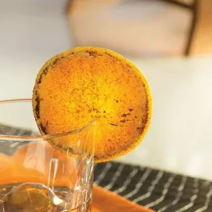 a glass of whiskey with an orange on the rim