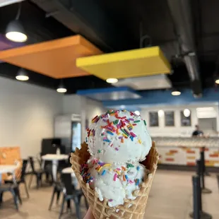 a hand holding an ice cream cone with sprinkles