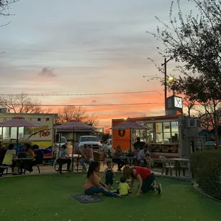 a group of people sitting on the grass in front of a food truck