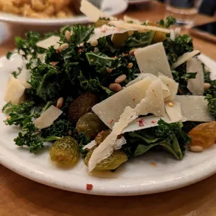 Kale Salad. Large $10. Pictured here is 1/2 serving. Pine nuts, golden raisins, shaved Parmesan, chili flakes, citrus vinaigrette.