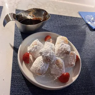 Beignets with powdered sugar, sliced strawberries and chocolate sauce for dipping.