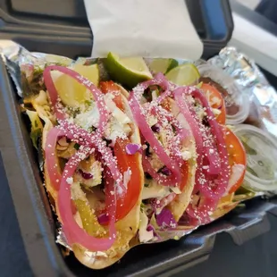a tray of tacos with onions, tomatoes, peppers, and cheese