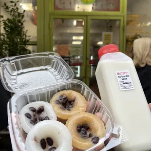 a person holding a container of doughnuts and a bottle of milk
