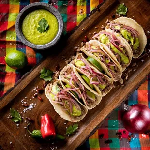 a wooden cutting board with tacos and guacamole