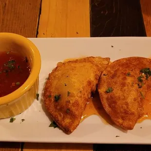 a white plate with two pieces of bread and a small bowl of sauce
