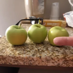 a person's hand reaching for three green apples
