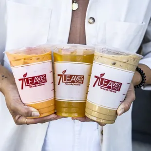 a woman holding three cups of iced coffee