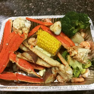 a tray of crab legs, broccoli, and corn