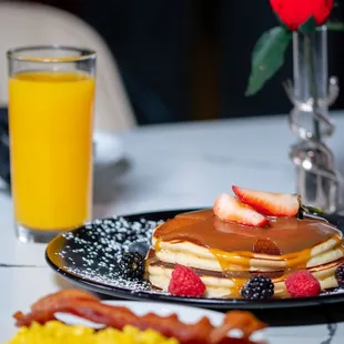 a plate of pancakes, bacon, eggs, and a glass of orange juice