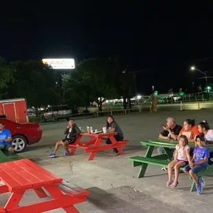 a group of people sitting at picnic tables in a parking lot