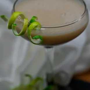 a cocktail in a martini glass with lime garnish