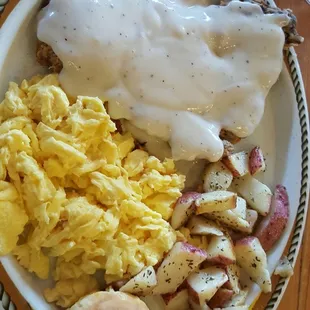 Chicken fried steak with scrambled eggs, potatoes, and a biscuit