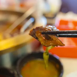 close up of chopsticks holding a piece of meat over a bowl of soup