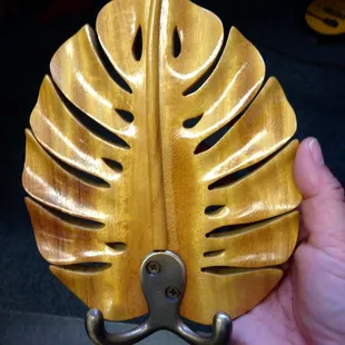 solid wood hand carved Monstera leaf with two brass hooks.  It has a hanging fixture attached to the back.  In dark wood, blonde, gold