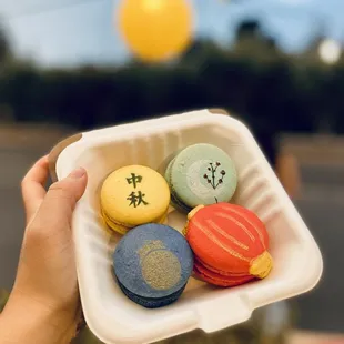 a person holding a container of macarons