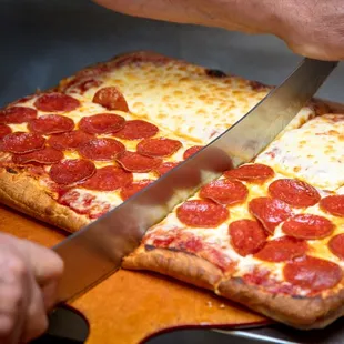 a person cutting a pepperoni pizza