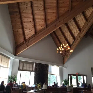 Dining room filled with people waiting, and a great view and ceiling being downplayed with dingy flooring/seating/table cloths.