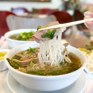 a person holding chopsticks over a bowl of soup