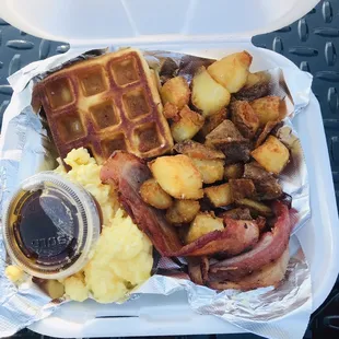 a waffle, bacon, potatoes, and syrup