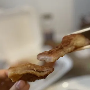 a hand holding a piece of bacon