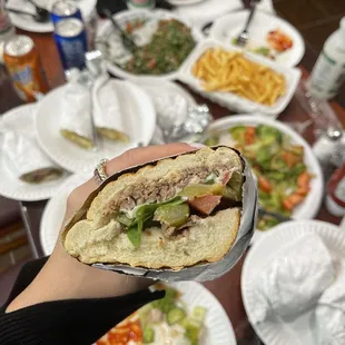 a person holding a sandwich over a table full of food