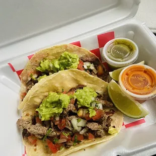 Dos tacos de asada con guacamole y salsa.