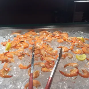 a tray of shrimp on ice with tongs
