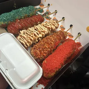 A blue takis, regular corn dog with ketchup, potato corn dog with spicy mayo, ramen corn dog with saracha hot Cheeto yellow cheese sauce