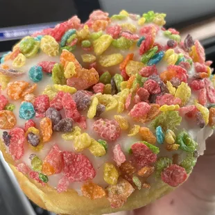 a hand holding a donut covered in cereal