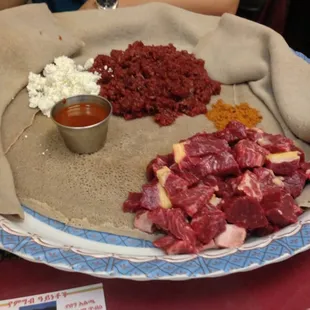 Tere sega on the bottom, kifto on the top, the cheese next to it, awaze in the tin sauce container and orange berbere.