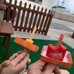 a person holding a popsicle with a popsicle sticking out of it